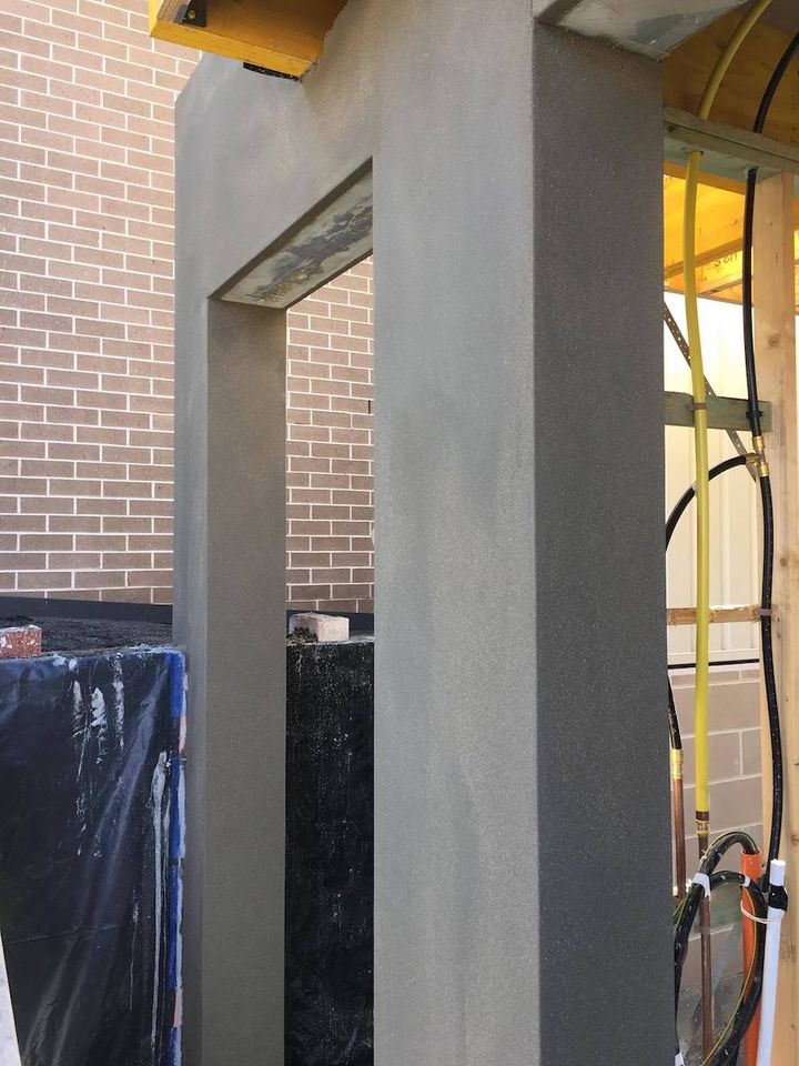A tall rendered column standing beside an existing brick wall on a build site