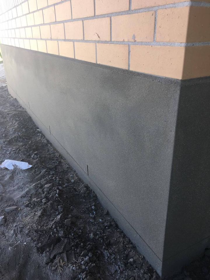 A rendered wall finished directly below an existing brick course, with a sharp top edge