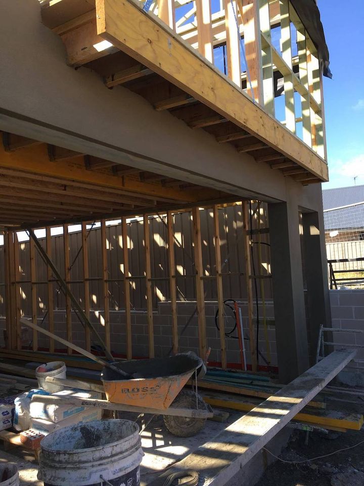 A rendered wall under a timber framed balcony on an active building site