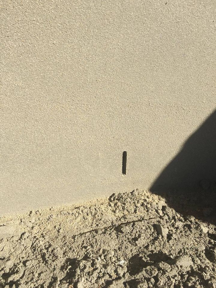 Close view of a freshly applied sand finish render, with sand heaped at the base of the wall