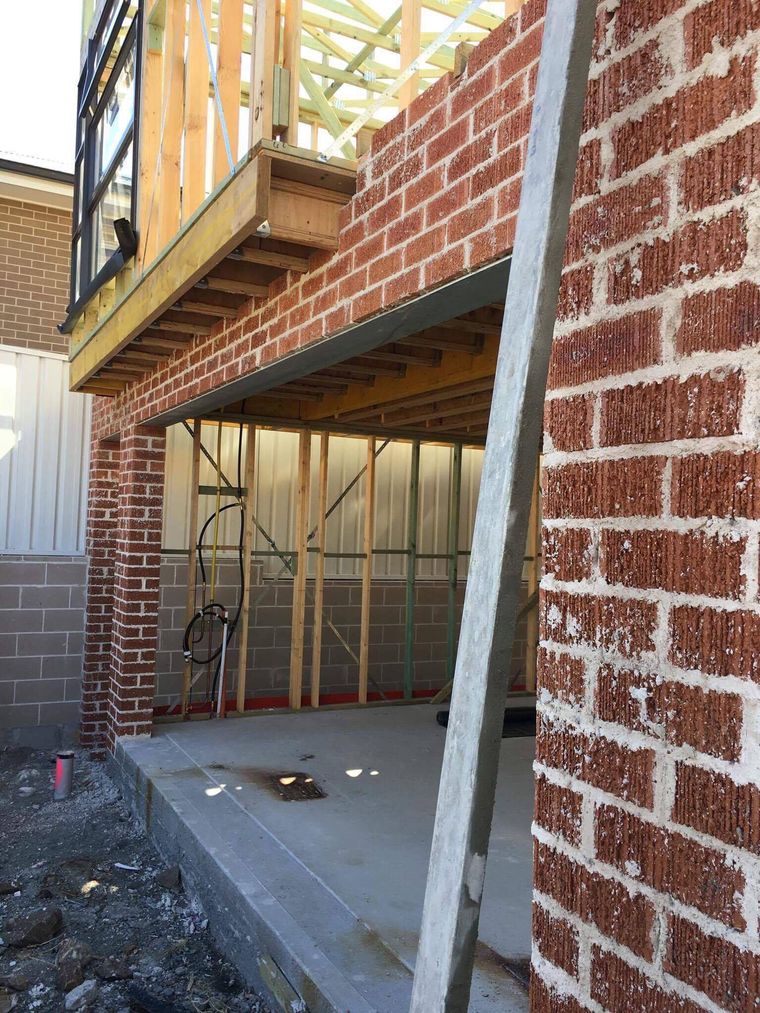 A raw brick wall beneath a timber balcony frame before rendering