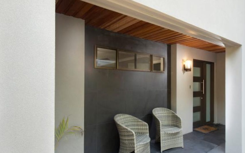 An entry portico with a charcoal rendered feature wall and a timber lined ceiling