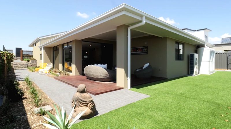 A rendered home with a covered alfresco opening onto a lawn and paved path
