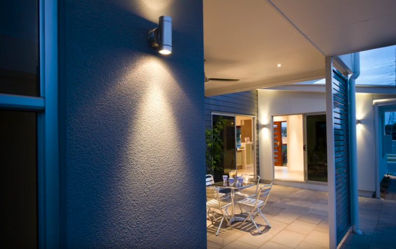 A deep blue rendered entry wall at dusk, lit from above, with the alfresco beyond