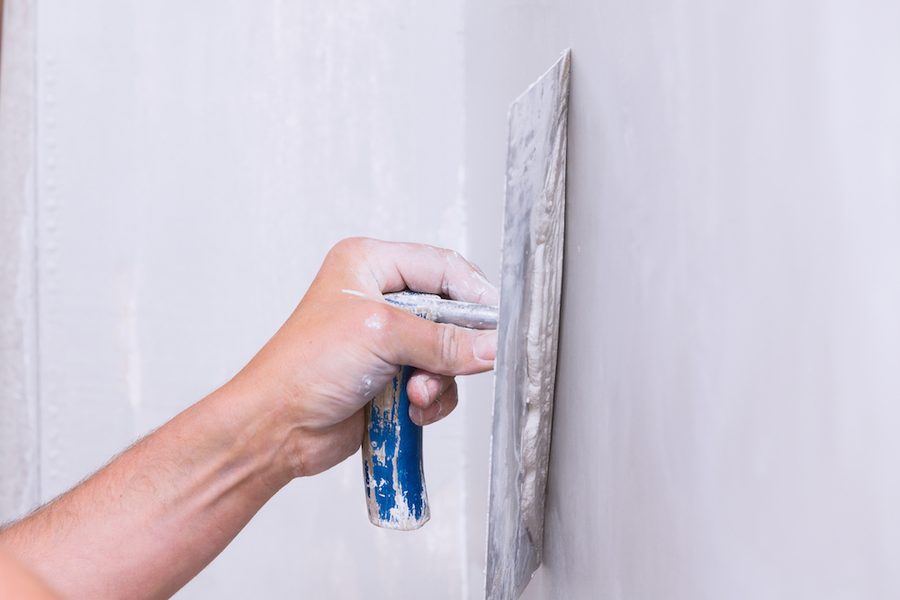 A hand drawing a steel trowel across freshly applied render