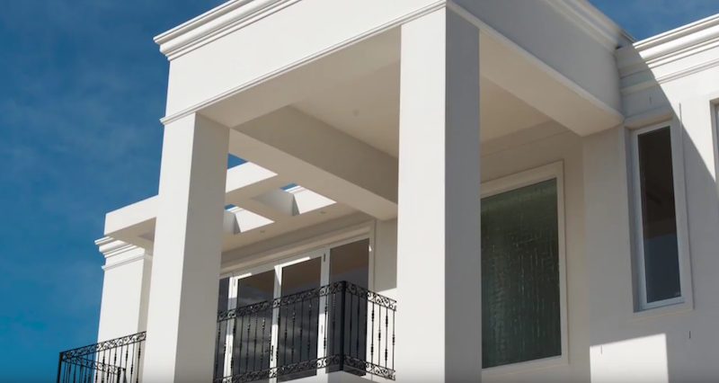A white rendered two storey home with square columns and a first floor balcony